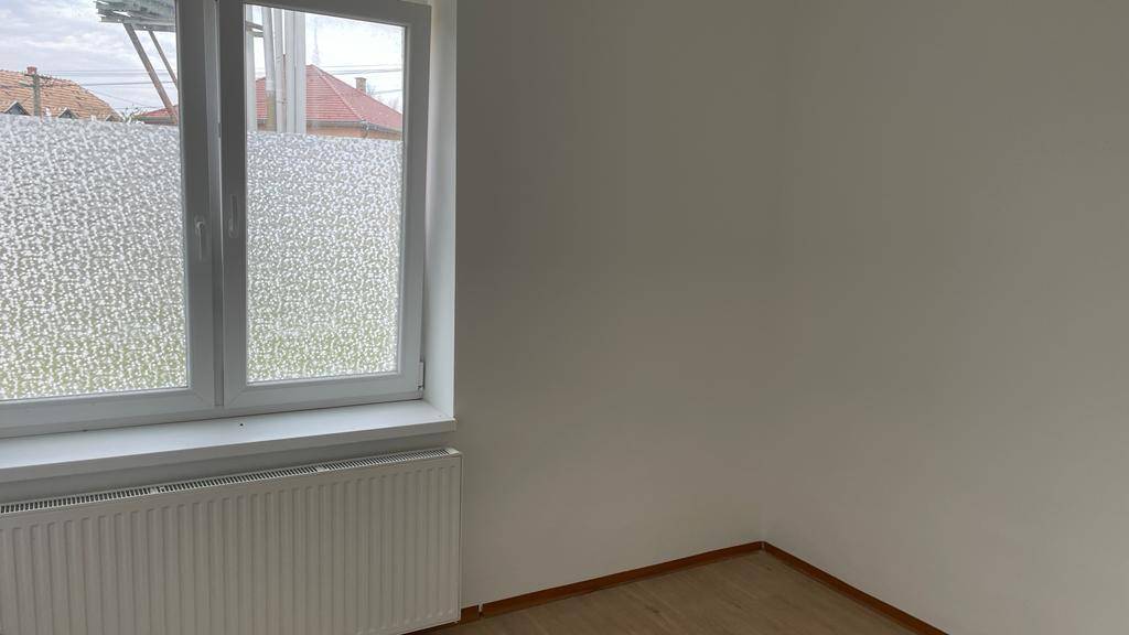 Heller Raum mit Laminatboden, weiß gestrichenen Wänden und einem großen Fenster mit Heizkörper.