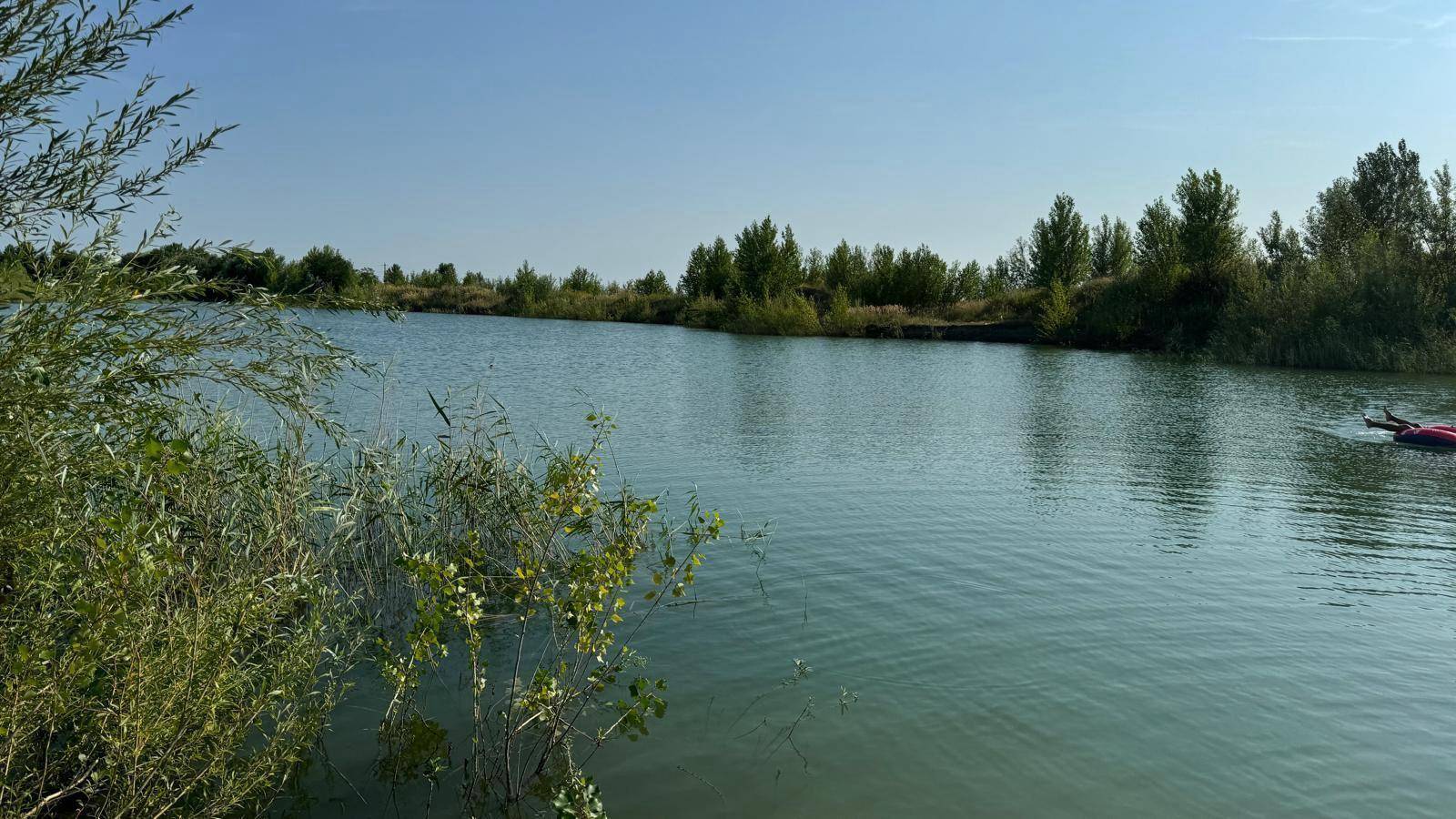 Person auf einem Schwimmreifen im ruhigen See, umgeben von grünen Bäumen am Ufer.