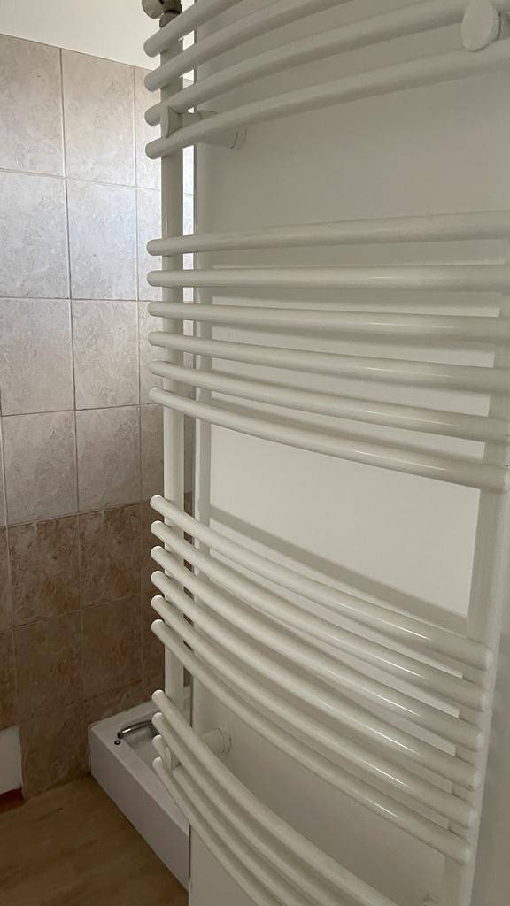 Moderner Handtuchheizkörper an einer gefliesten Wand in einem Badezimmer.