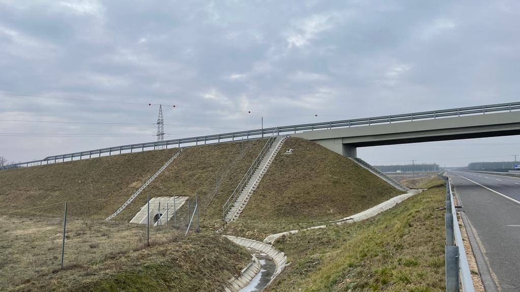Autobahnüberführung mit begrünter Böschung und Entwässerungssystem am Straßenrand.
