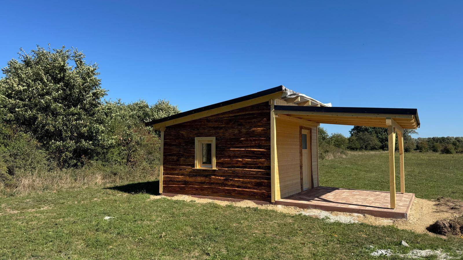 Eine kleine Holzhütte mit überdachtem Eingangsbereich in einer ländlichen Umgebung.
