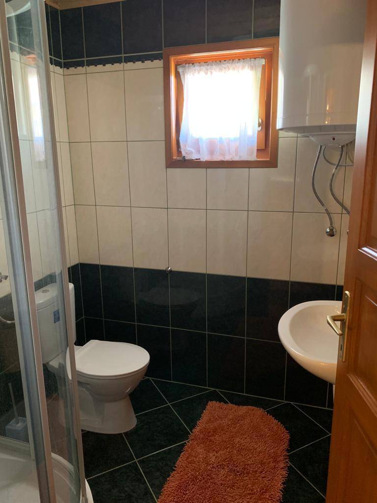 Badezimmer mit schwarz-weißen Fliesen, Dusche, wandhängendem WC, Waschbecken und Fenster.