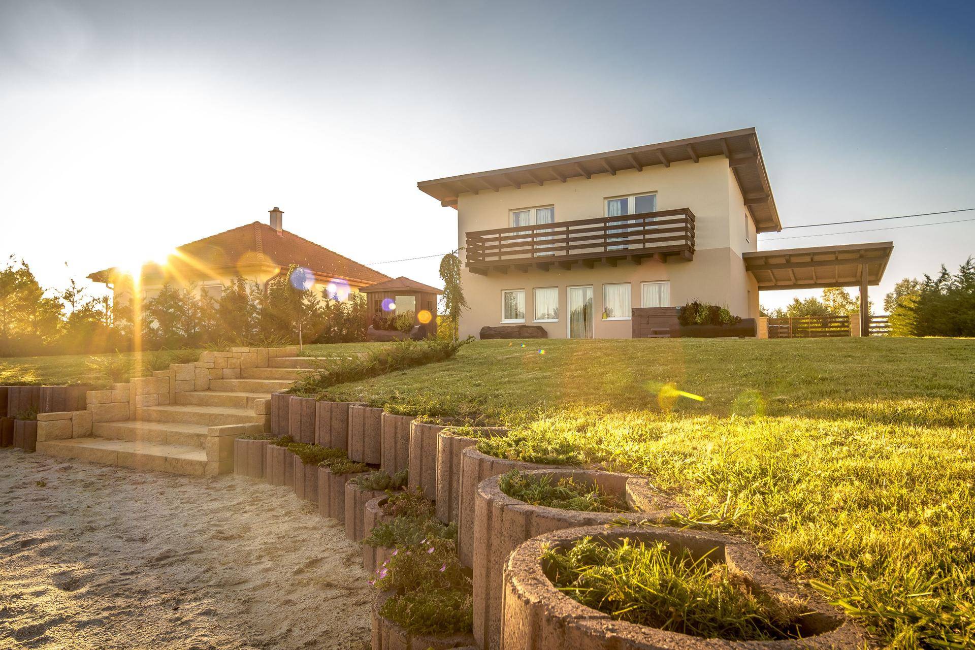Hausfassade mit Balkon und weitläufigem Gartenbereich bei Sonnenuntergang.