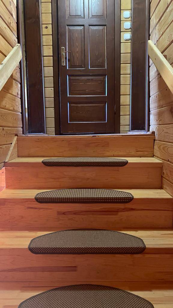 Detailansicht der Holztreppe und der Eingangstür, alles in warmen Holztönen gehalten.