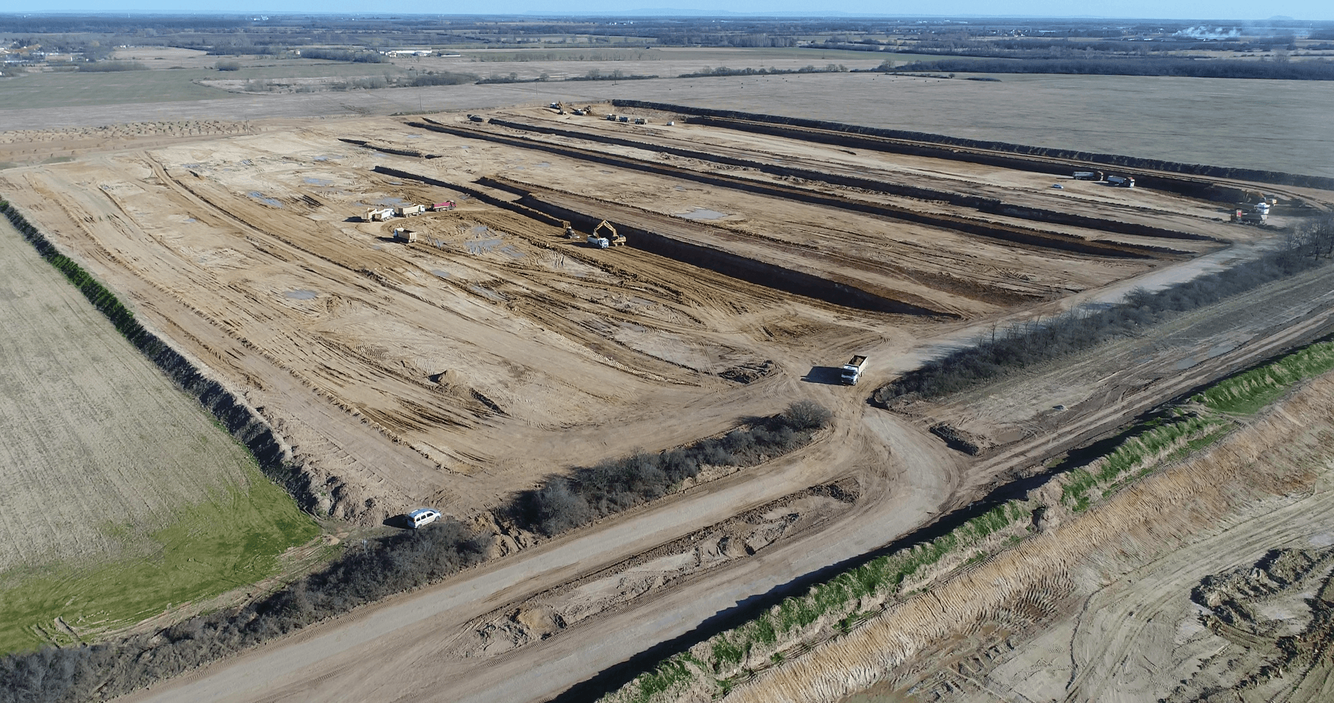Luftaufnahme einer großen Baustelle mit mehreren ausgehobenen Gräben und Baumaschinen in der Landschaft.