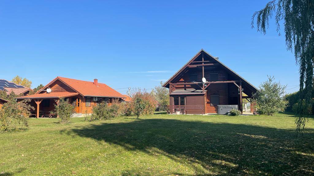 Weitläufiger Gartenbereich mit Holzhaus und weiteren Gebäuden in der Ferne unter blauem Himmel.