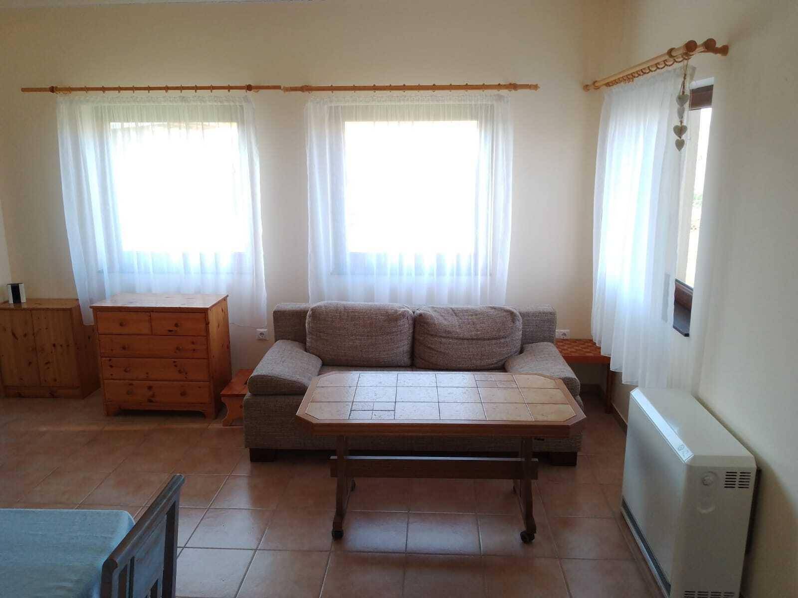 Heller Wohnbereich mit Sofa, Kommode und Fliesenboden, gut beleuchtet durch Fenster.