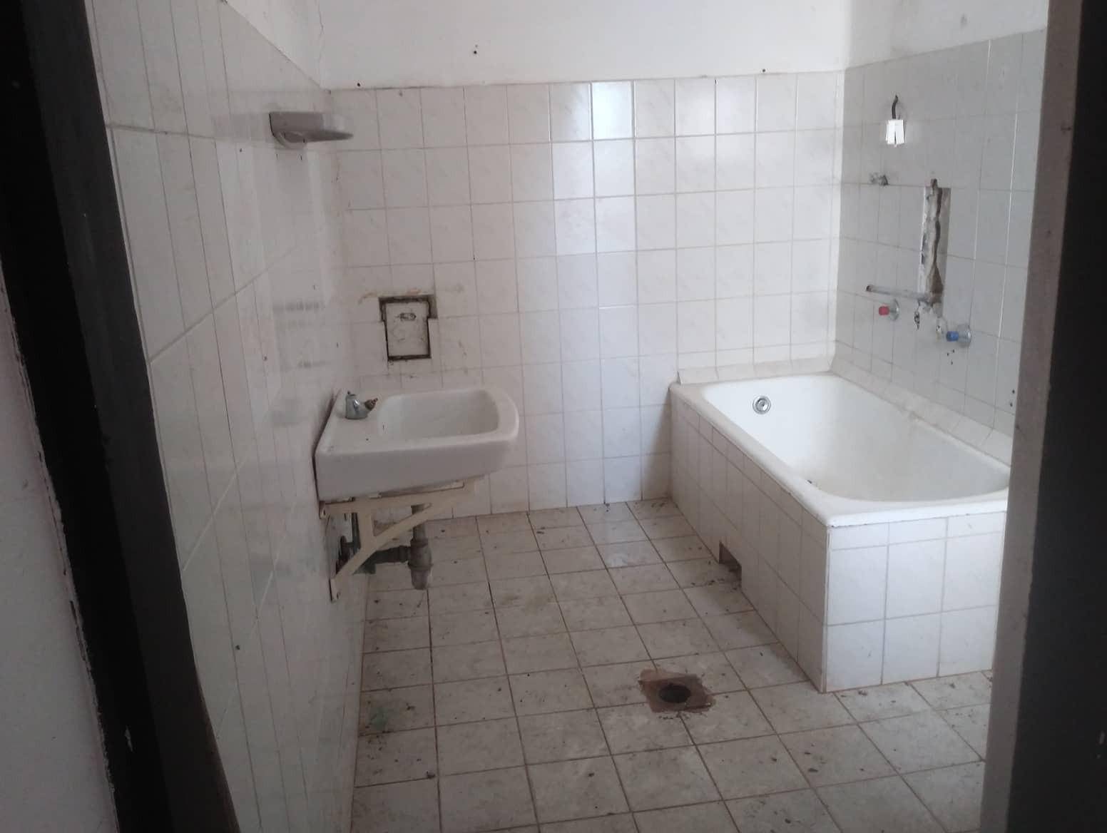Altes Badezimmer mit weißen Fliesen, Badewanne und Waschbecken, das dringend renoviert werden muss.