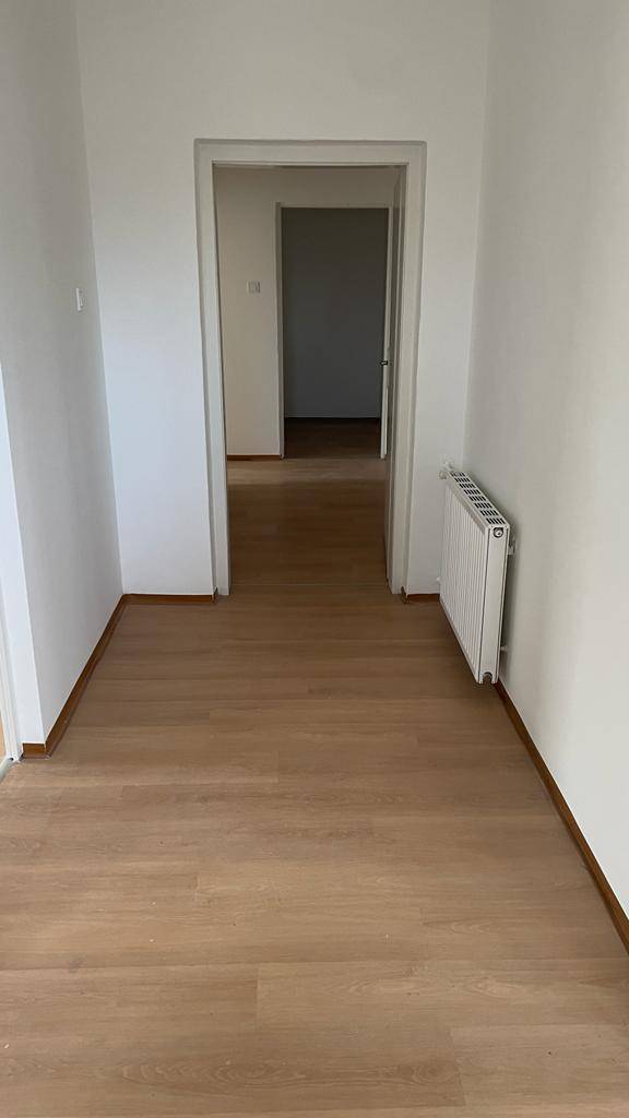 Langer Flur mit Laminatboden, weißen Wänden und einem Heizkörper.