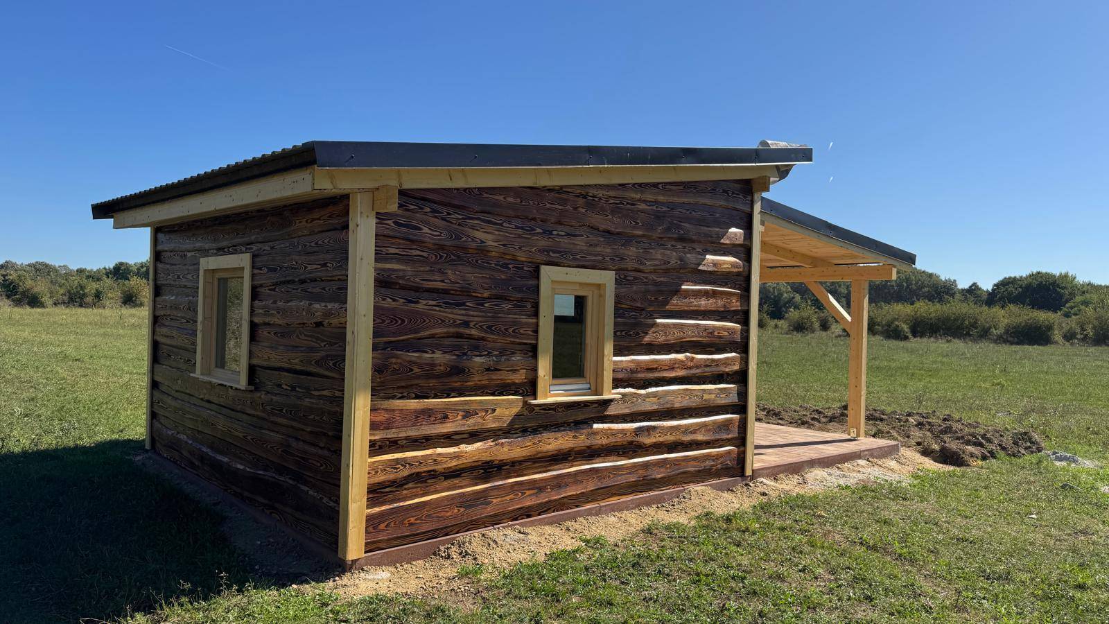 Seitenansicht der rustikalen Holzhütte mit Fenstern und dunkler Holzverkleidung.