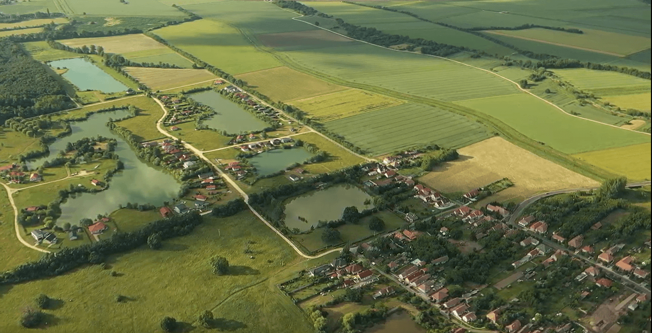 Weitläufige Luftaufnahme der Seenlandschaft mit angrenzenden Feldern und Siedlungen unter klarem Himmel.