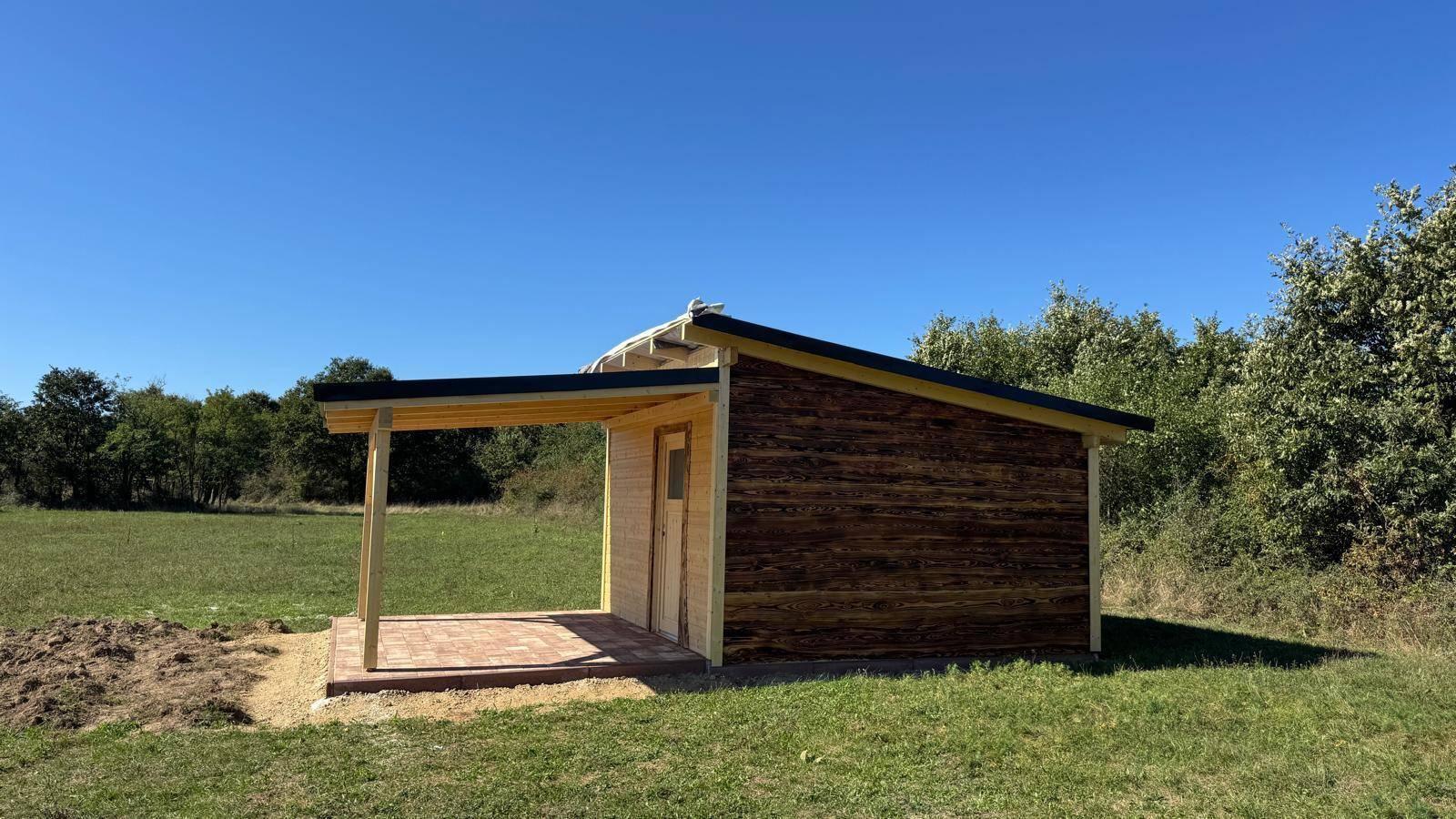 Die kleine Holzhütte mit überdachter Terrasse, eingebettet in die weite Naturlandschaft.