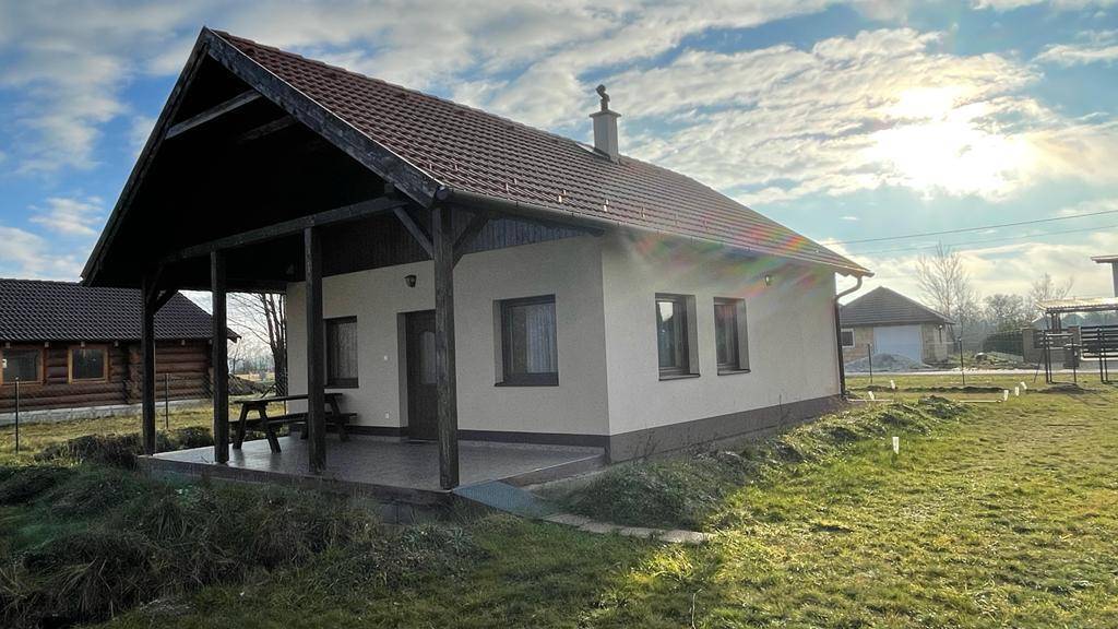 Freistehendes Haus mit Ziegeldach und überdachtem Eingangsbereich in sonniger Landschaft.