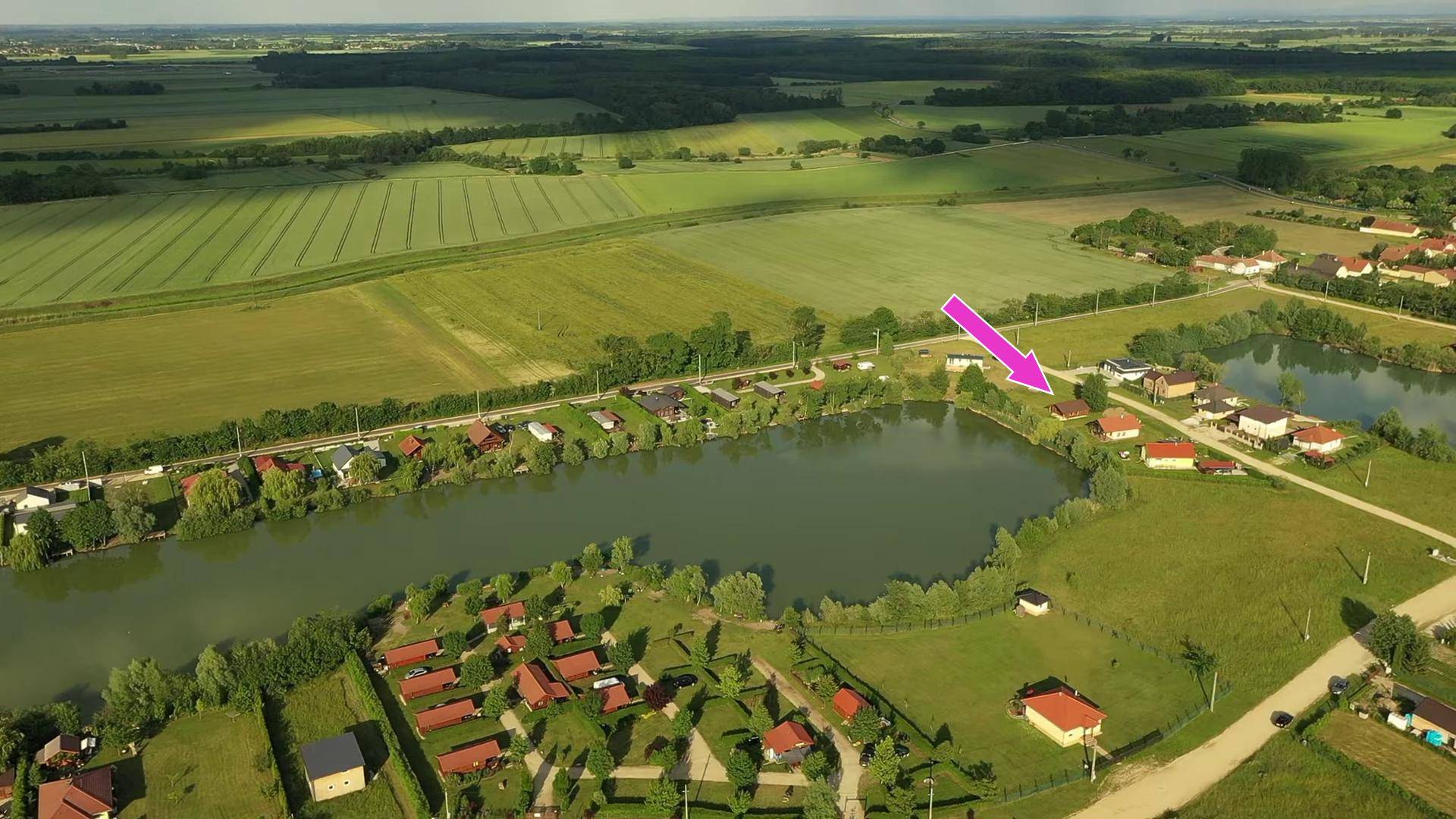 Luftaufnahme einer ländlichen Siedlung am See mit Feldern und einem Pfeil, der auf ein Grundstück zeigt.