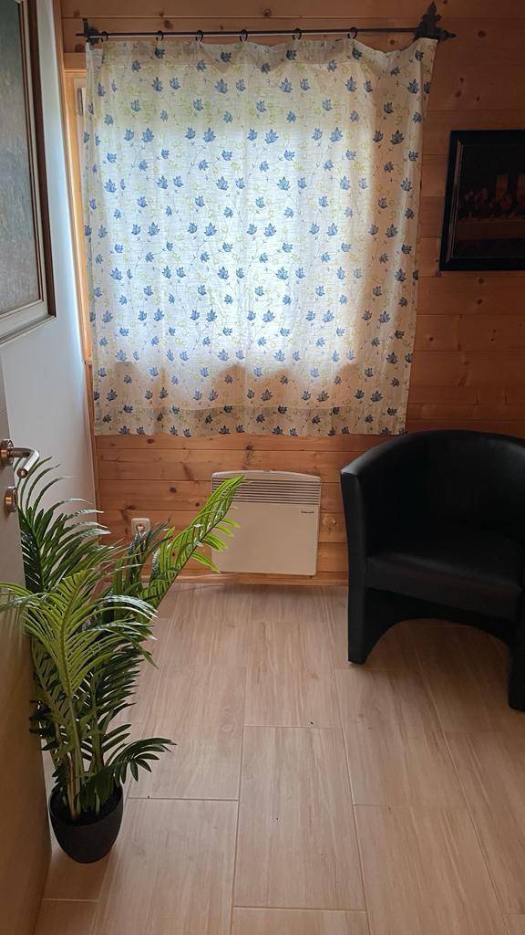 Fenster mit Vorhang und einem Sessel vor einer Holzwand.