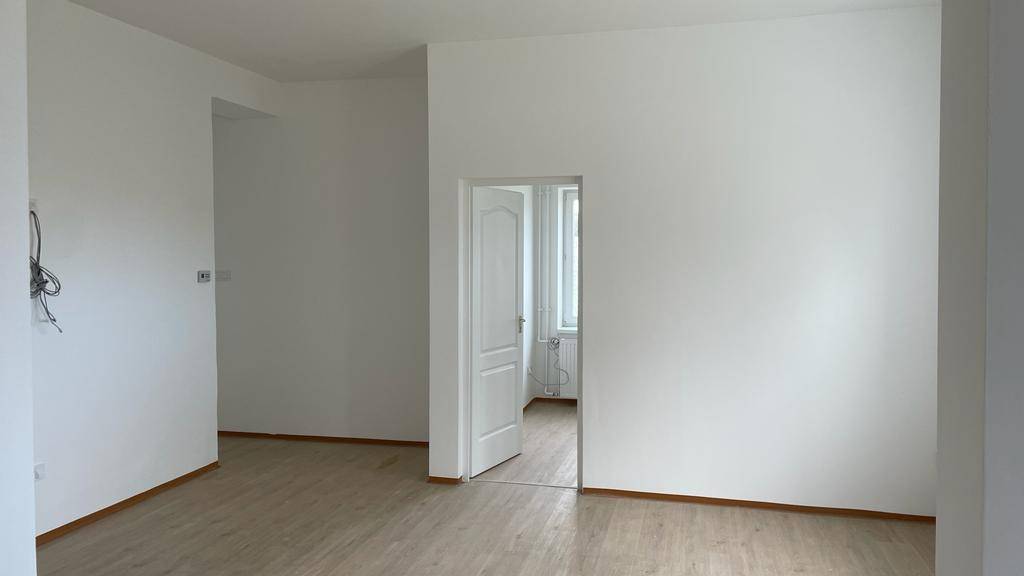 Heller Raum mit weißen Wänden, Laminatboden und einer Tür zu einem weiteren Zimmer.
