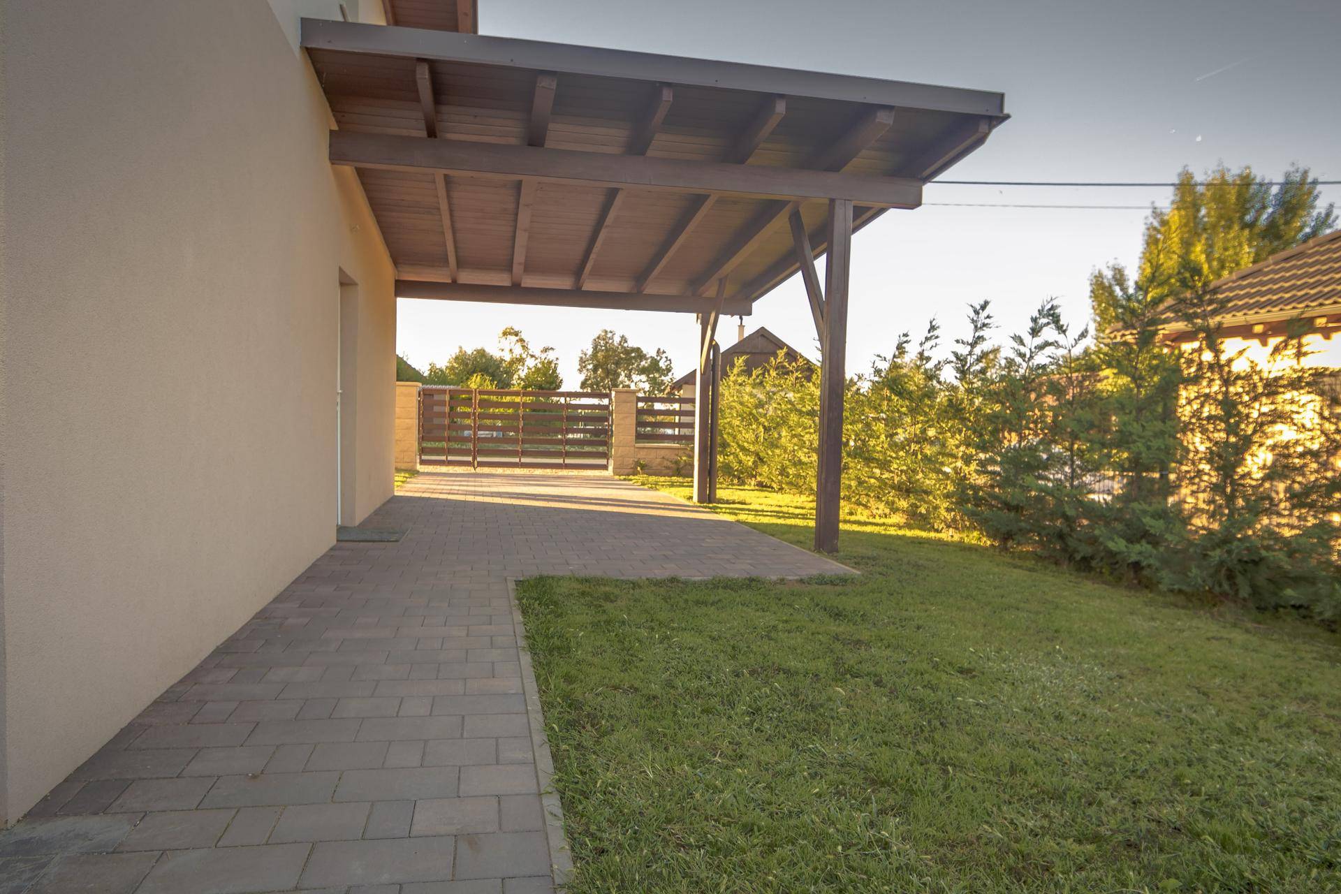 Carport und gepflasterter Bereich neben dem Haus mit Rasenfläche.