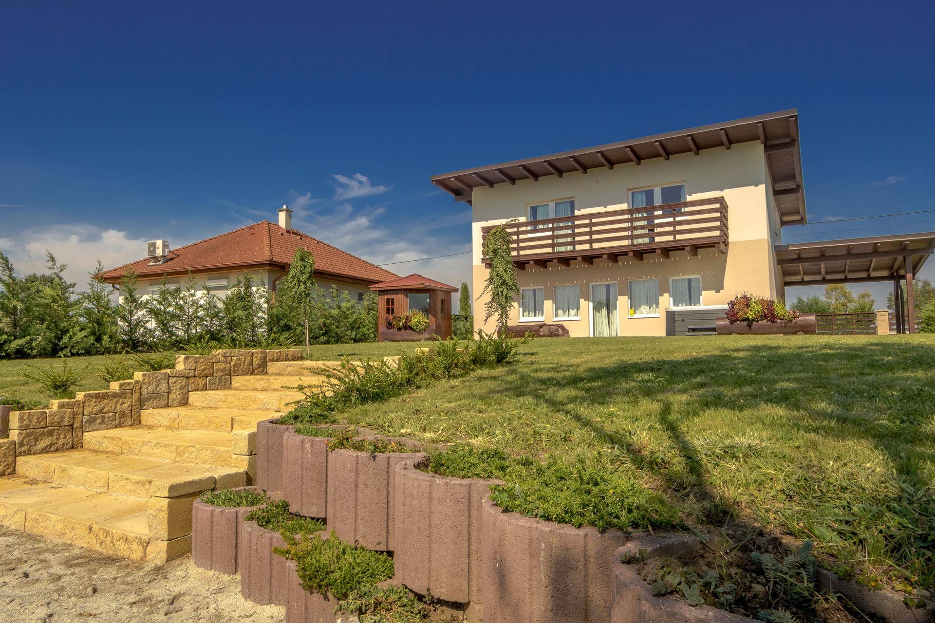 Hausfassade mit Balkon und weitläufigem Gartenbereich mit Steintreppe.