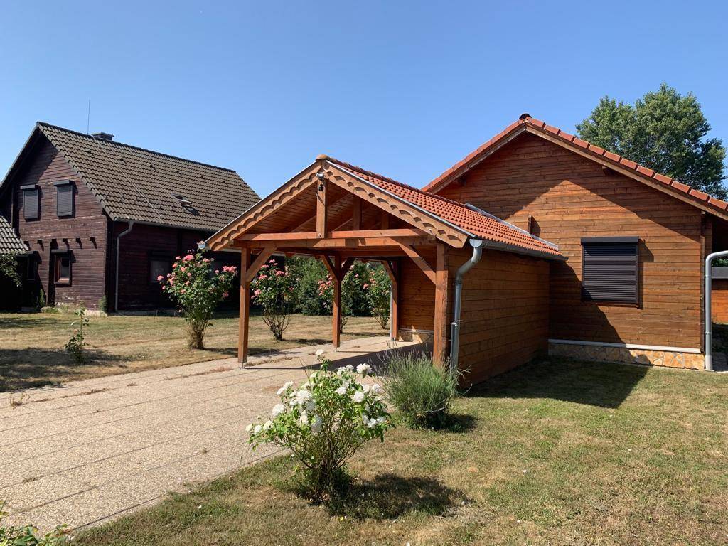 Zwei Holzhäuser mit Carport und Gartenbereich unter blauem Himmel, zeigen die ländliche Umgebung.