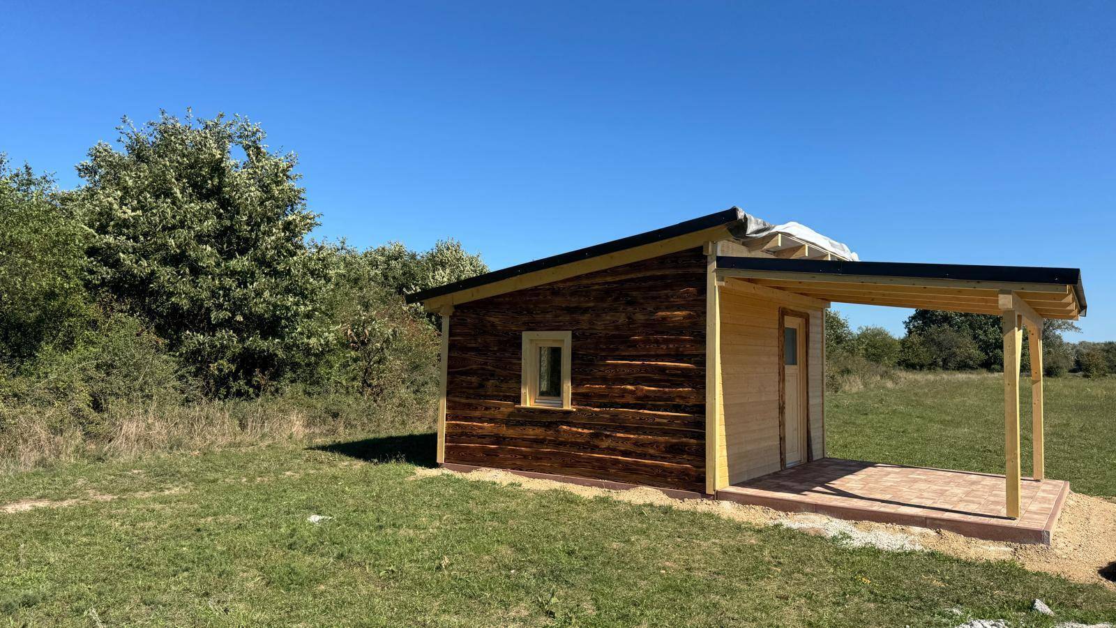 Frontansicht der Holzhütte mit einem Fenster und dem überdachten Eingangsbereich.