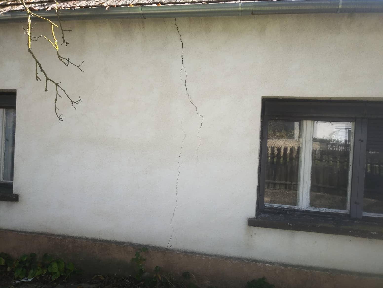 Fassade eines Hauses mit sichtbaren Rissen und einfachen Fenstern, die auf Sanierungsbedarf hindeuten.