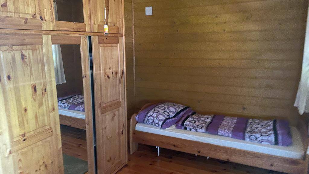 Schlafzimmer mit Einzelbett und großem Holzschrank mit Spiegeltür, alles in Holz gehalten.