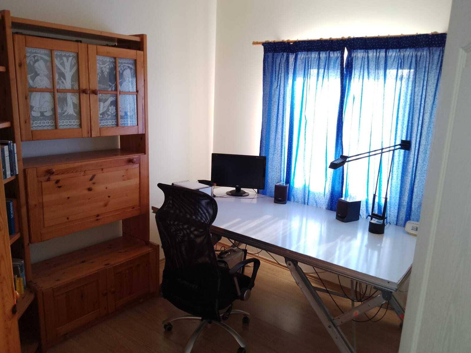 Arbeitszimmer mit großem Schreibtisch, Computer und blauen Vorhängen am Fenster.