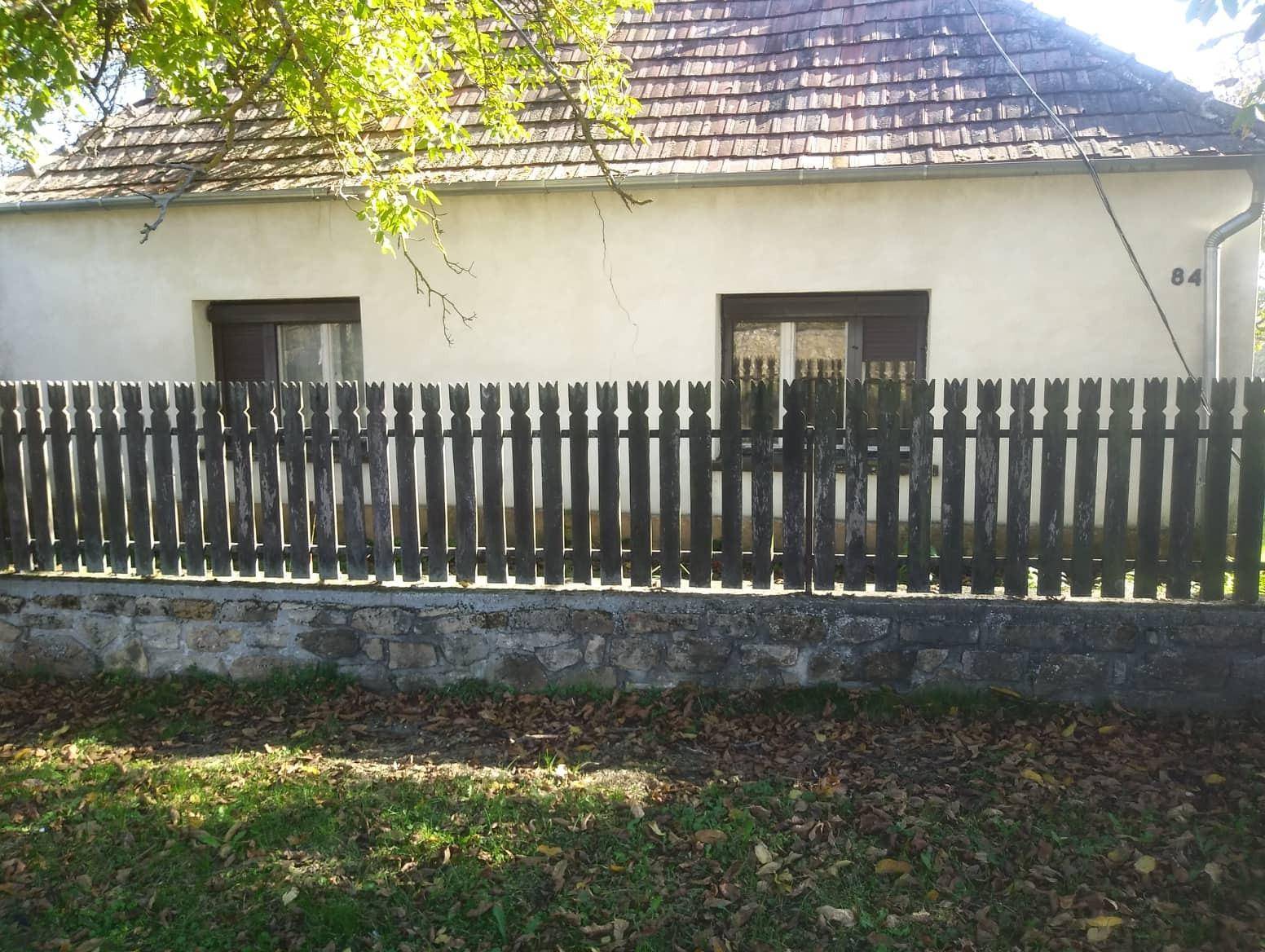 Altes Haus mit Holzzaun und Ziegeldach, umgeben von Herbstlaub und einem Hausnummernschild.