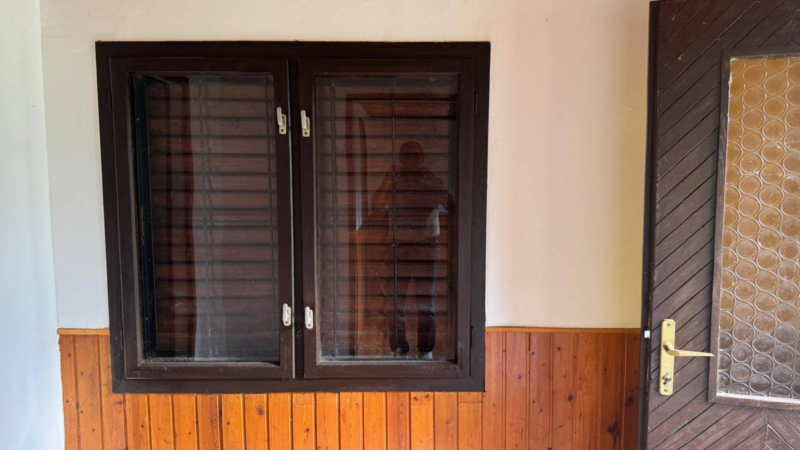Nahaufnahme eines Fensters mit braunem Rahmen und einer Holztür mit Glaseinsatz.