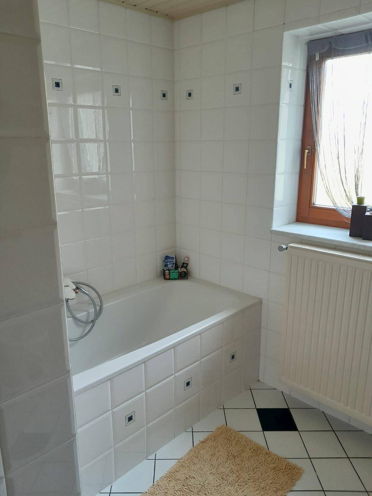 Badezimmer mit Badewanne, weißen Fliesen, Fenster und Heizkörper.