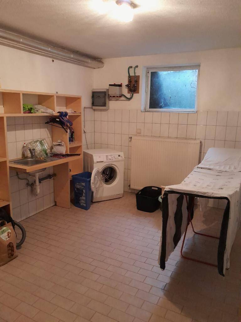 Funktionale Waschküche im Keller mit Waschmaschine, Spülbecken und Fliesenboden.