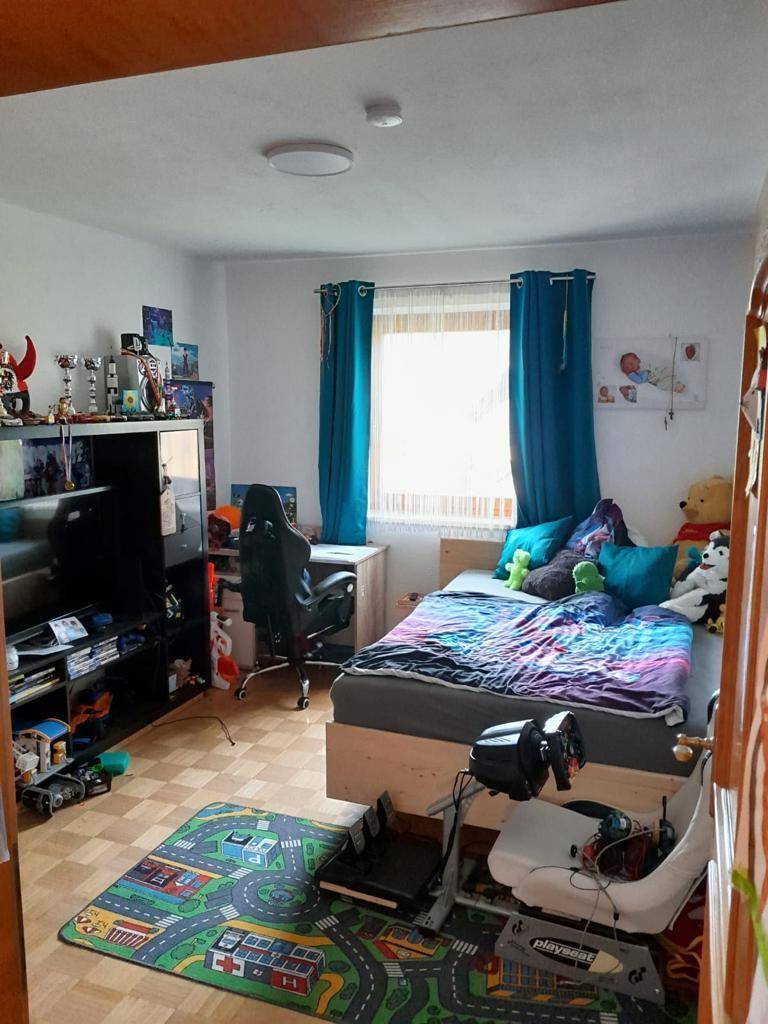 Helles Kinderzimmer mit Bett, Schreibtisch, bunten Vorhängen und Laminatboden.