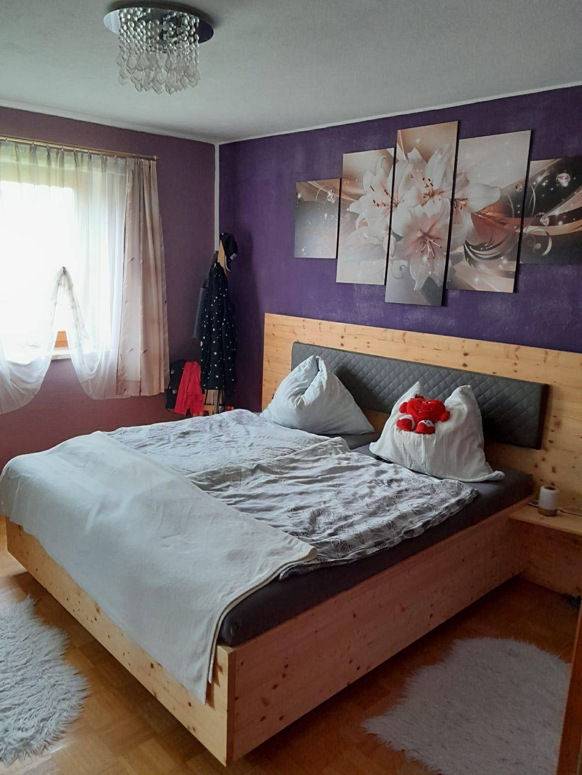 Modernes Schlafzimmer mit Doppelbett, lila Akzentwand und großem Wandbild.