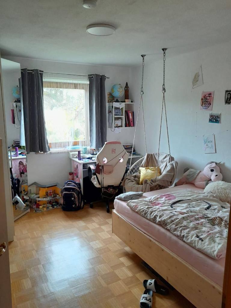 Freundliches Kinderzimmer mit Bett, Schreibtisch, Hängesessel und Laminatboden.