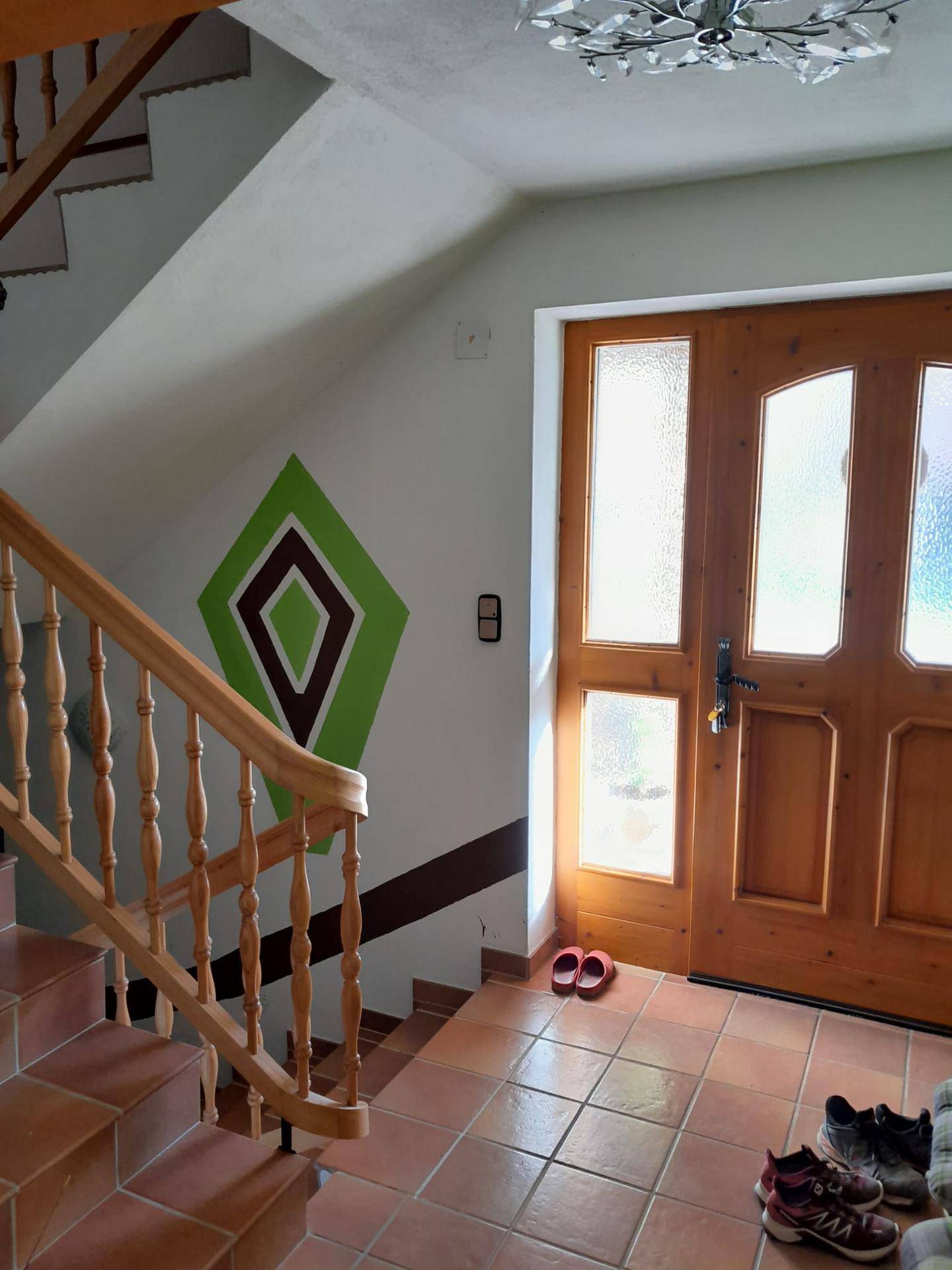 Eingangsbereich mit Holztreppe, Terrakotta-Fliesen und Haustür mit Glaseinsätzen.