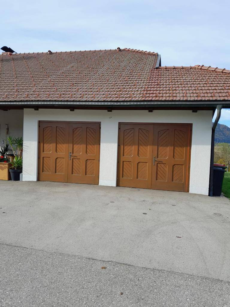 Zwei braune Garagentore an der Hausfassade mit Ziegeldach und Einfahrt.