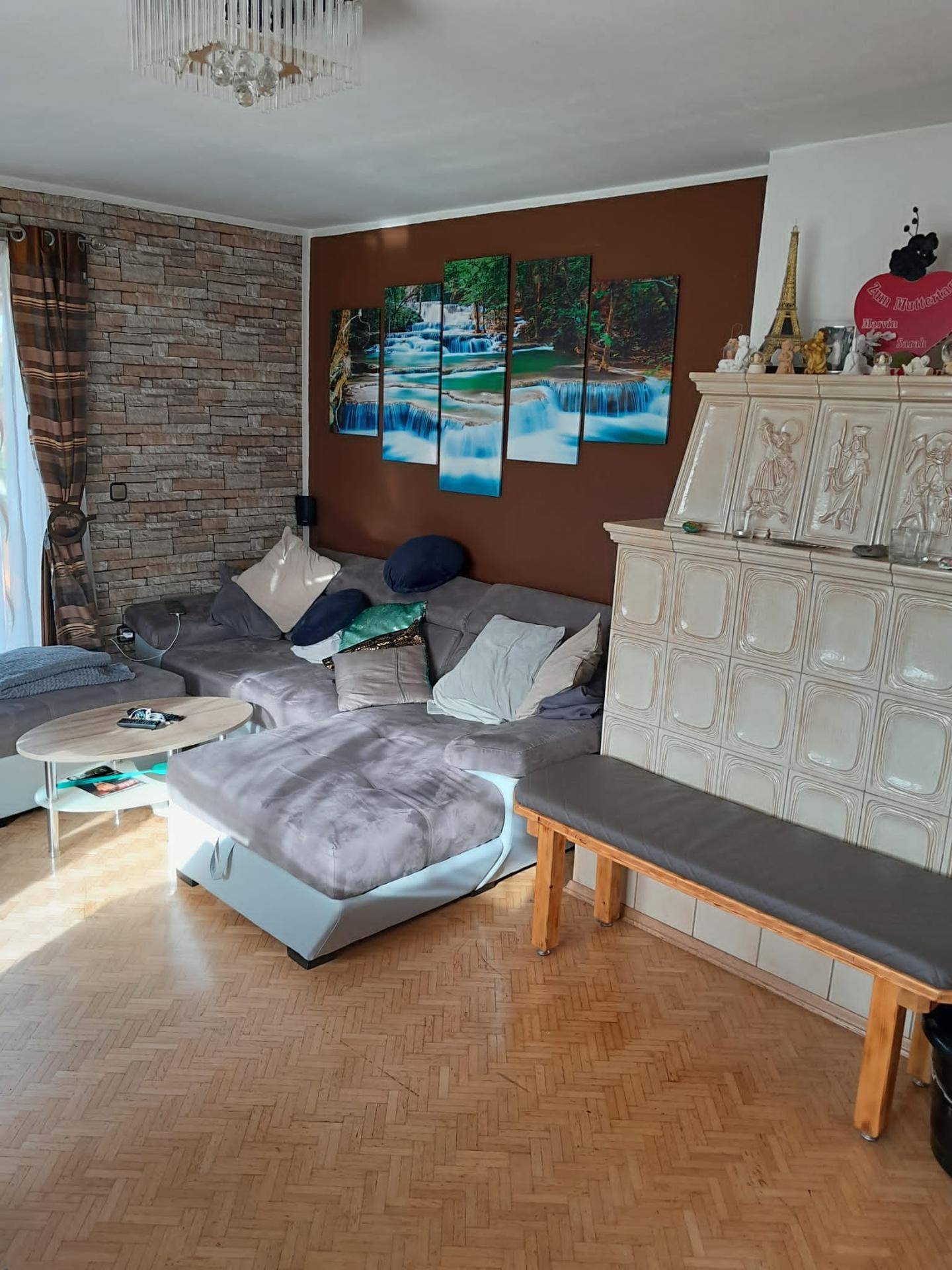 Gemütliches Wohnzimmer mit großem Sofa, traditionellem Kachelofen und Laminatboden.