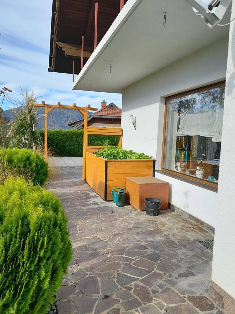 Gepflasterter Gartenbereich mit Hochbeet, grünen Büschen und Blick ins Grüne.
