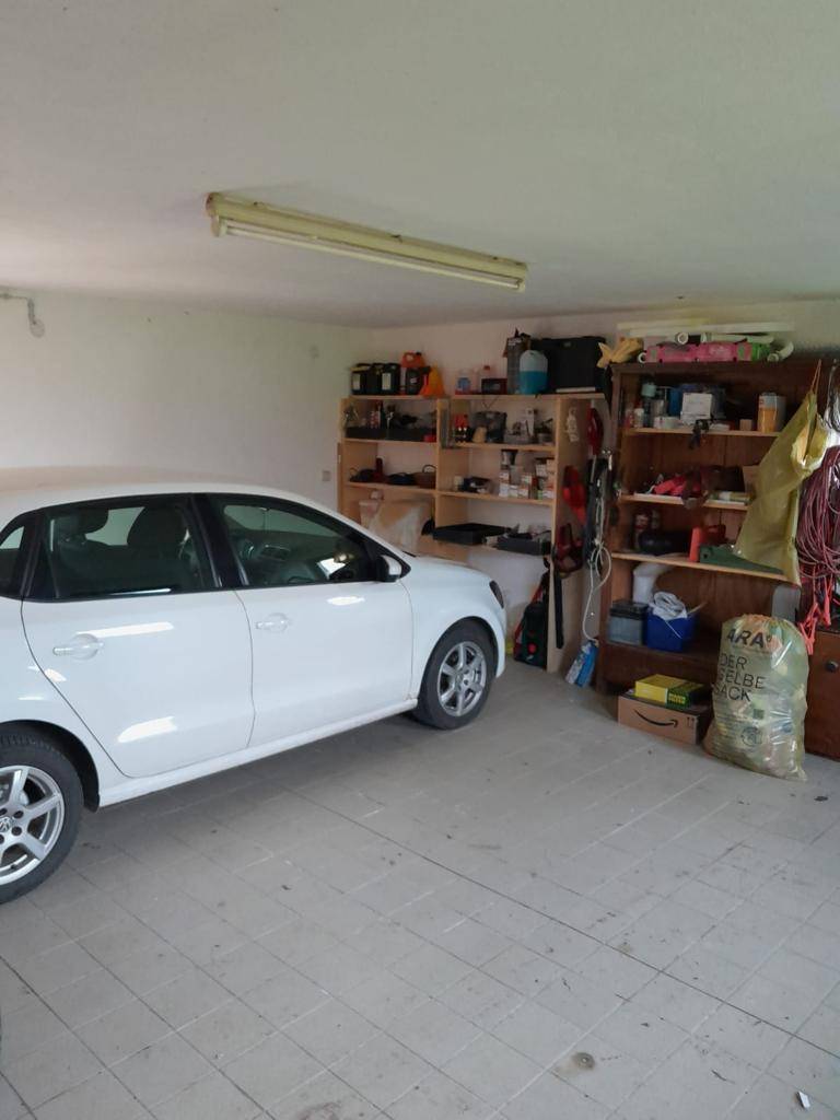 Geräumige Garage mit einem geparkten Auto, Regalen und Fliesenboden.