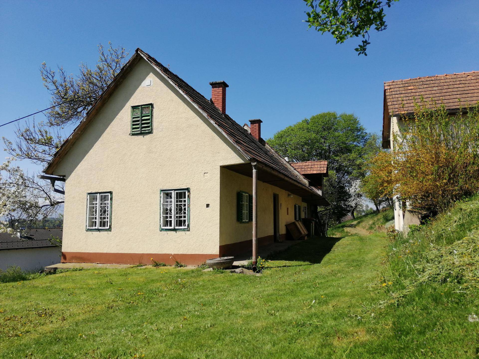 Seitenansicht des Hauses mit beiger Fassade, grünen Fensterläden und Ziegeldach.