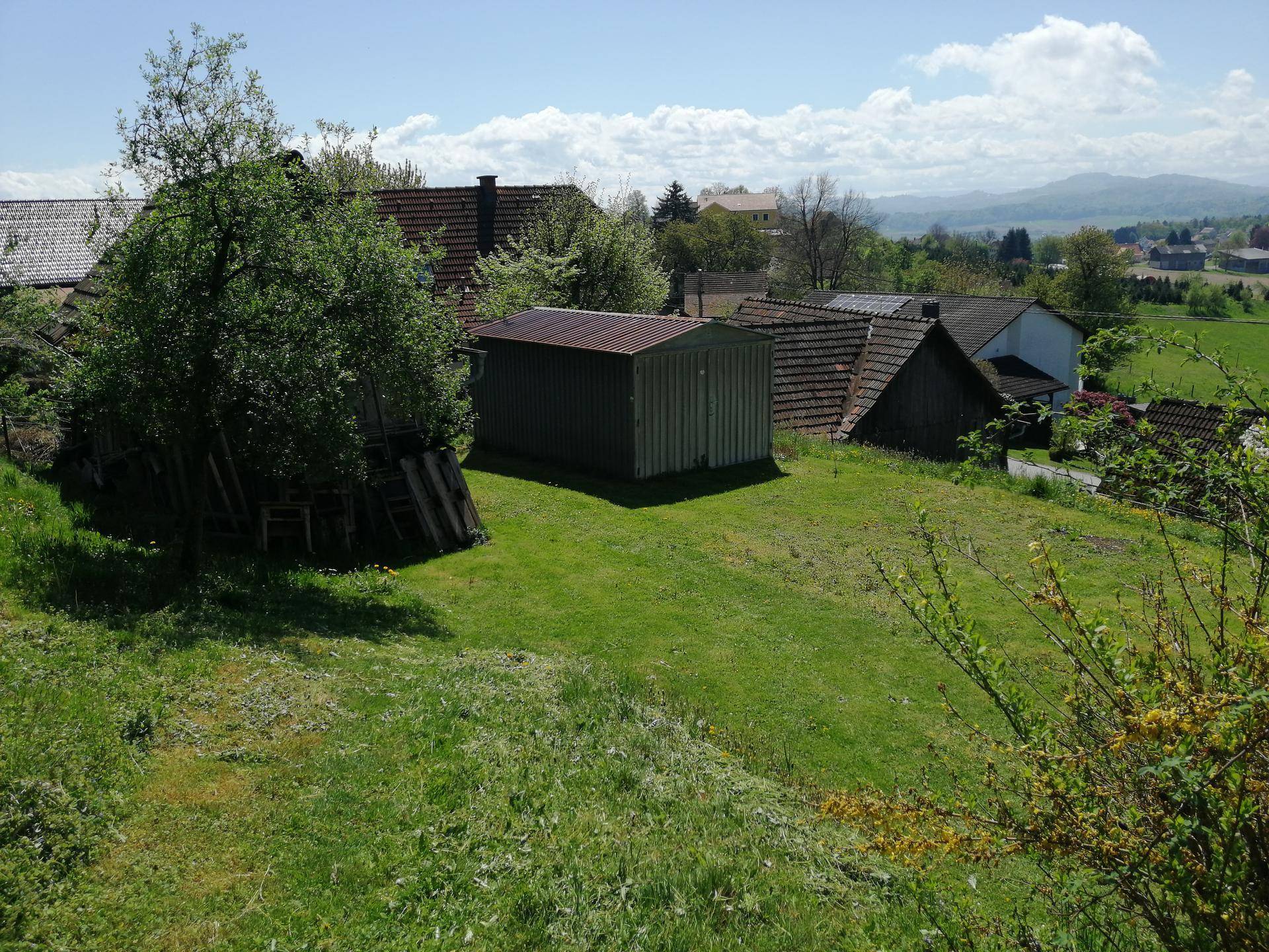 Gartenbereich mit Schuppen und Blick auf die umliegende Landschaft und Berge.