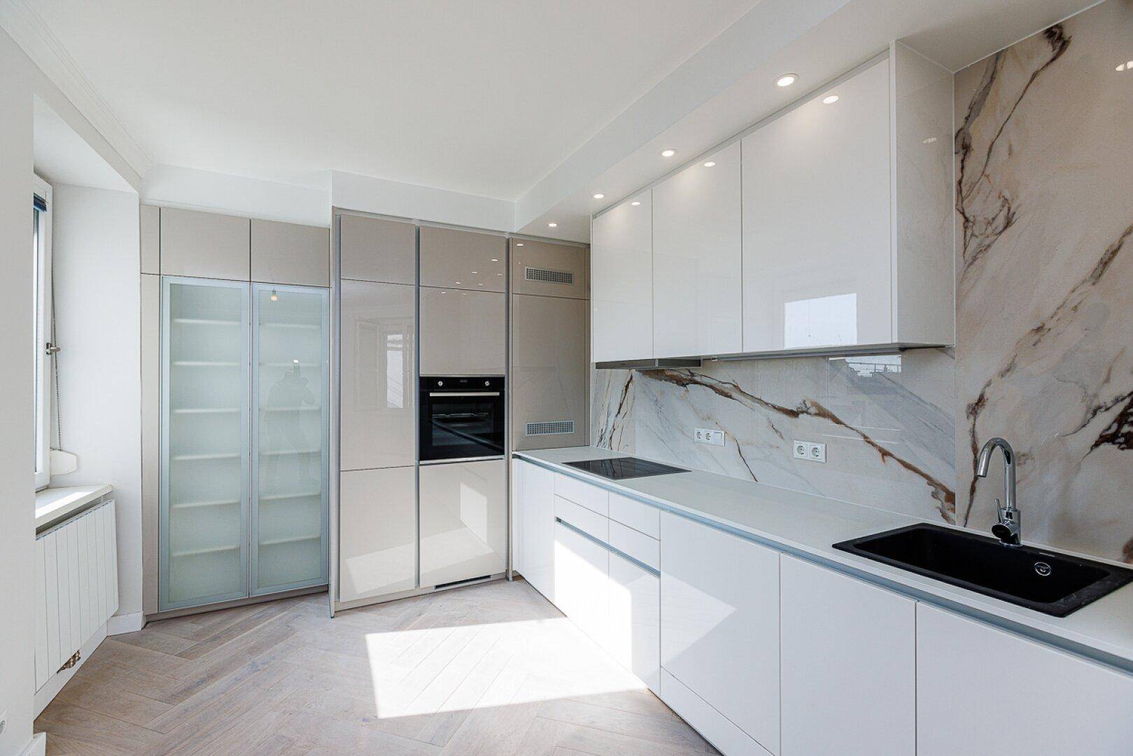 Moderne Einbauküche mit glänzenden Fronten, Marmor-Rückwand und integrierten Geräten.