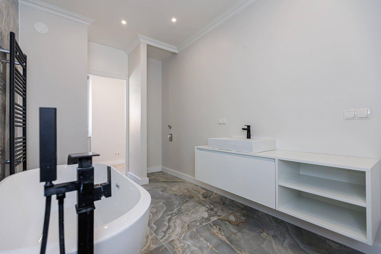 Modernes Badezimmer mit freistehender Badewanne, schwebendem Waschtisch und dunklen Armaturen.