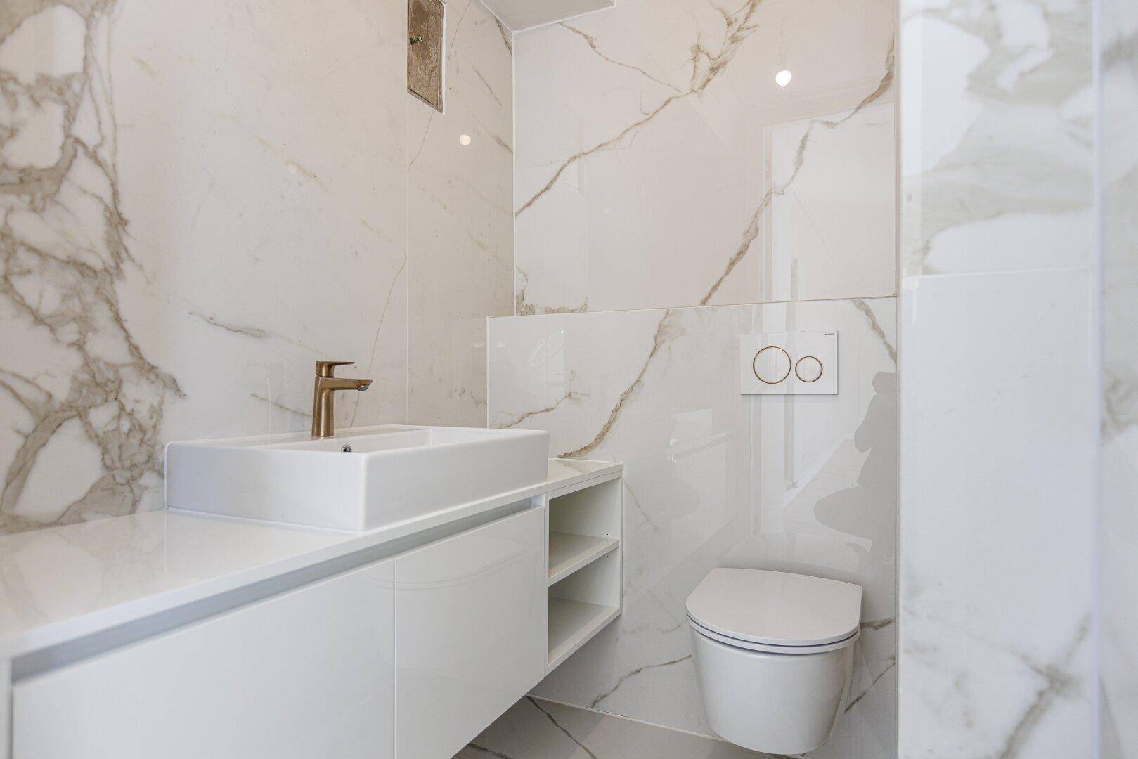 Modernes WC mit Marmorfliesen, schwebendem Waschtisch und eleganten goldenen Armaturen.