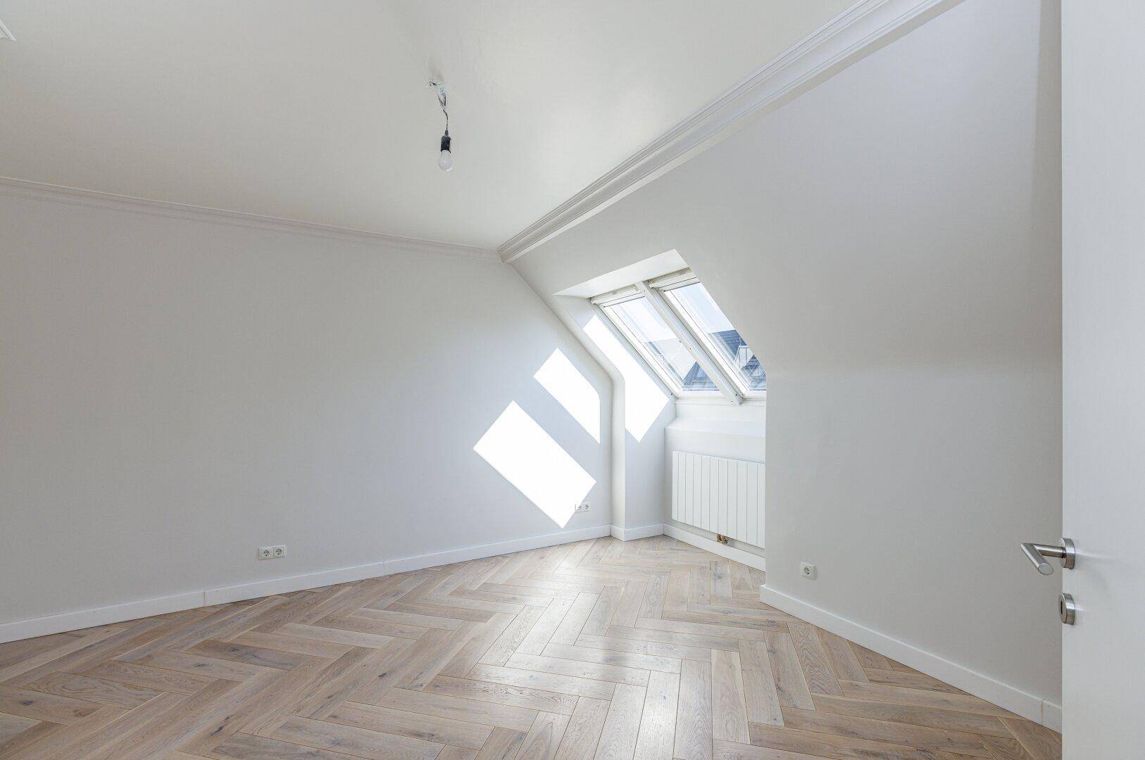 Helles Schlafzimmer mit Fischgrätparkett, Dachfenster und schrägen Wänden, bereit zur Einrichtung.
