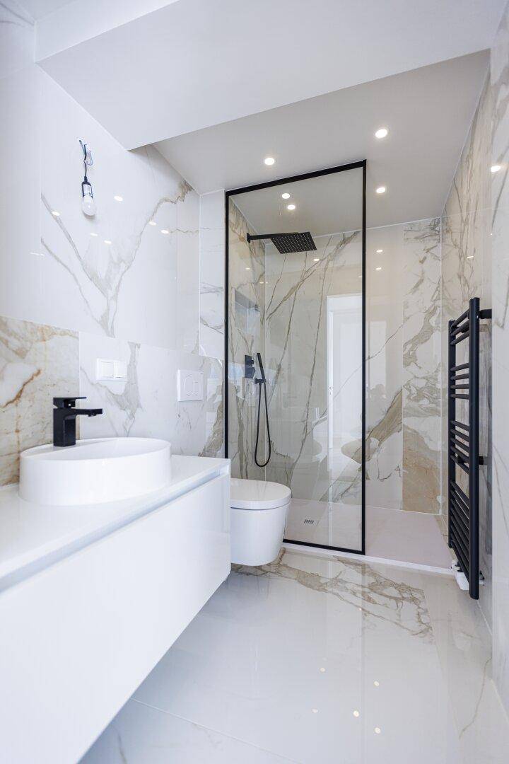 Stilvolles Badezimmer mit großformatigen Marmorfliesen, begehbarer Dusche und modernem Waschtisch.