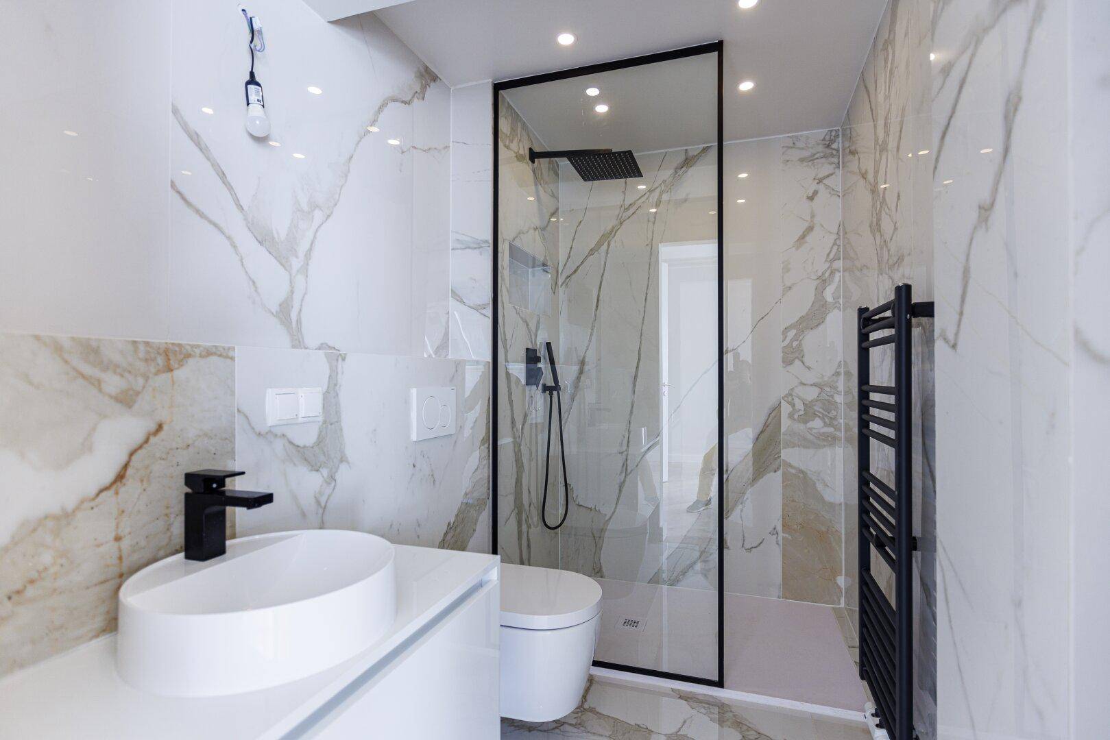 Elegantes Badezimmer mit Marmorfliesen, moderner begehbarer Dusche und stilvollen schwarzen Armaturen.