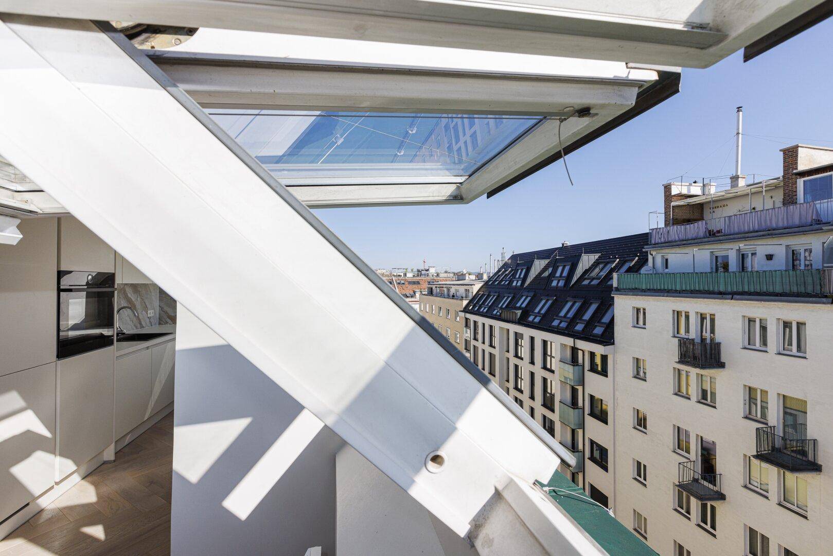 Blick aus einem Dachfenster auf die umliegenden Dächer und die städtische Architektur.