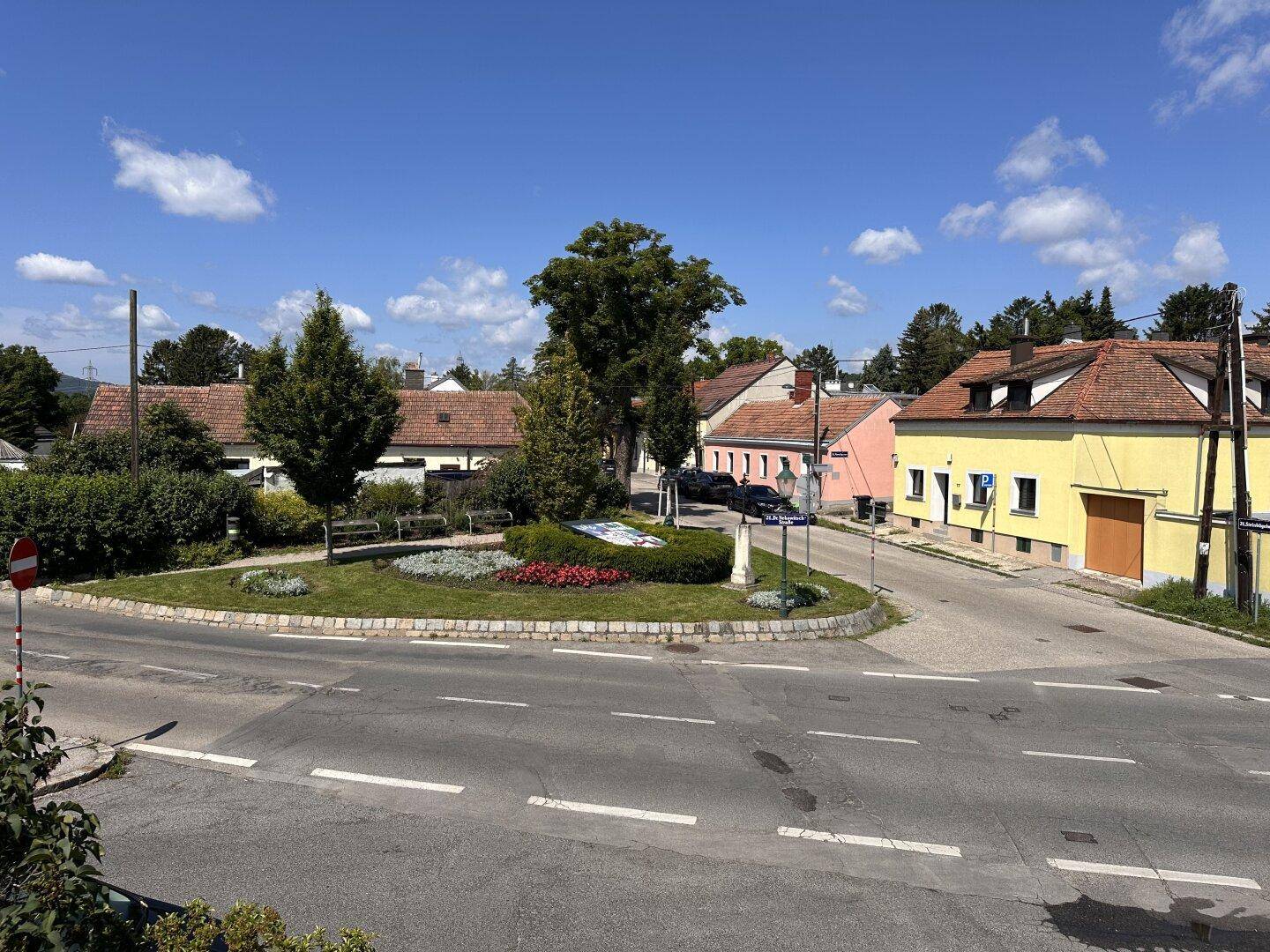 Blick auf eine ruhige Wohngegend mit einem Kreisverkehr und traditionellen Häusern unter blauem Himmel.