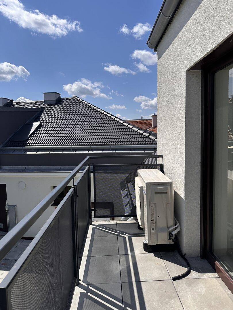 Kleiner Balkon mit Fliesenboden, Metallgeländer und Klimaanlage mit Blick auf die Dächer.